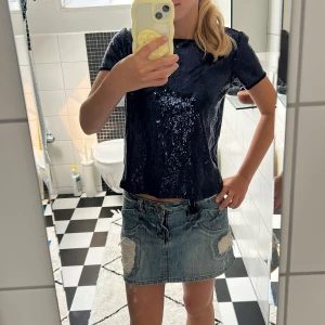 Mörkblå paljettopp från Lindex - Säljer en mörkblå topp från Lindex med massor av glittrande paljetter. T-shirten har korta ärmar och rund halsringning. Perfekt för dig som vill sticka ut med en riktigt snygg och glittrig look. 