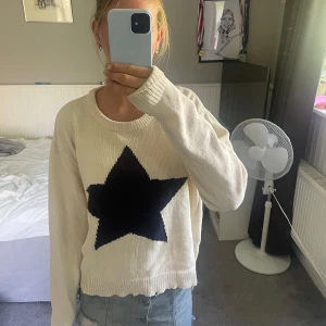 Beige stickad tröja med svart stjärna från Nelly  - Superfin beige stickad tröja med en stor svart stjärna framtill. Tröjan har rund halsringning och långa ärmar, använd en gång köpt på Nelly storlek L men passar mig som har S på tröjor 