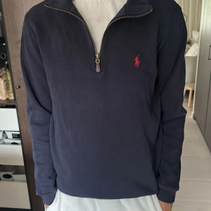 Mörkblå half zip från Polo Ralph Lauren - Snygg mörkblå långärmad tröja från Polo Ralph Lauren med half zip och klassisk röd logga broderad på bröstet. Tröjan är i bomull och har en normal passform, perfekt till en chill och stilren look. Nypris 2000kr.