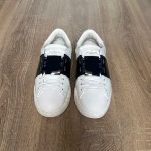Valentino Open sneakers svart/vit  - Sänker pris vid snabb affär, Snyggaste Valentino Open sneakers i vitt skinn med bred svart läderdetalj över snörningen. Klassisk rund tå, vita snören och platt sula. Diskreta nitar baktill ger extra edge. Perfekta för dig som gillar stilrena och lyxiga sneakers.