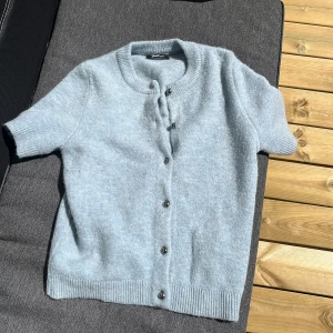 Ljusblå kofta från Gina Tricot - Superfin ljusblå kofta från Gina Tricot med korta ärmar och rund hals. Koftan är stickad och har knappar framtill. Använd 2 gånger. Passar både xs/s