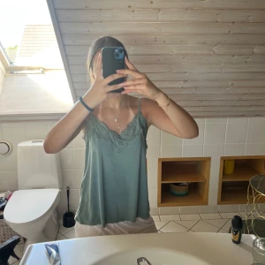 Grön linnetopp med spetsdetaljer - Snygg ljusgrön linnetopp med tunna axelband och v-ringning dekorerad med spets. Toppen har en avslappnad passform och är perfekt för varma dagar. Materialet känns mjukt och svalt mot huden. Enkel att styla med både jeans och kjol💕💕