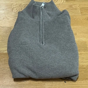 Beige  ribbad half zip stickad tröja - Snygg beige stickad tröja med ribbad struktur och half zip-dragkedja i halsen. Tröjan har lång ärm och hög krage. 