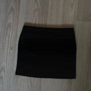 Svart kortkjol med slits - Enkel och stilren svart kortkjol med liten slits framtill. Kjolen har en tight passform och är perfekt att matcha med en crop top eller oversized hoodie. Materialet känns mjukt och stretchigt.