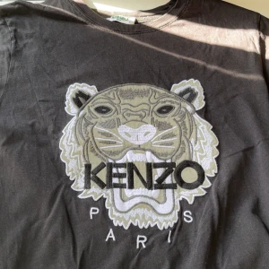 Svart Kenzo t-shirt med tigertryck - Svart t-shirt från Kenzo med ikoniskt broderat tigerhuvud och texten 'KENZO PARIS' på bröstet. Klassisk rund halsringning och korta ärmar. Sitter perfekt och är true to size 