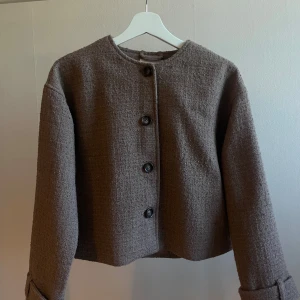 Beige/brun  jacka från Nelly - Stilren beige/brun jacka från Nelly med grovstickad struktur och rund halsringning. Perfekt för dig som gillar en enkel men trendig look. Jackan är oanvänd så i mycket bra skick! 🥰
