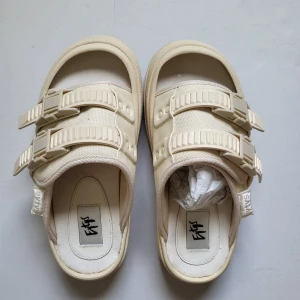 Beige sandaler från Eytys med spännen / Eytys Capri - Chunky sandaler från Eytys i beige med två breda remmar och coola plastspännen. Snygg platt sula med hjärtdetalj undertill och öppen tå. Ovandel i textil och syntet, perfekt för en avslappnad och trendig look.