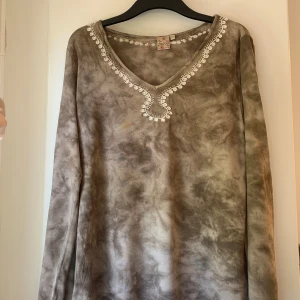 Tiediy tröja - Långärmad tröja från Indiska i batikmönster. V-ringad hals med vit broderad kant och små pärlor. Tröjan har två små lappade hål som syns i både första och sista bilden.