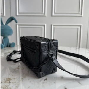 Svart Louis Vuitton axelväska i skinn - Säljer en svart axelväska från Louis Vuitton i boxig form med präglat monogrammönster. Väskan har robusta metallhörn, grov kedjerem och dragkedja med LV-detalj. Tillverkad i grained skinn och har en cool, modern vibe.