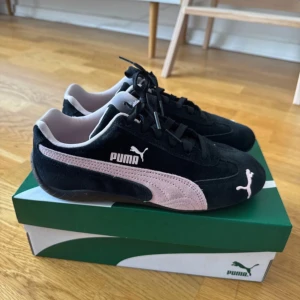 Svarta och rosa sneakers från Puma speedcats OG - Snygga svarta sneakers från Puma med ljusrosa detaljer och klassisk logga på sidan och tån. Skorna har mockaöverdel, svart snörning och låg profil. Perfekta för dig som vill ha en sportig och stilren look med en touch av färg. Oanvönda