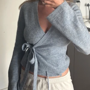 Ljusblå omlottkofta från Gina Tricot - Supermjuk ljusblå omlottkofta från Gina Tricot med knyt i sidan och v-ringad hals. Koftan är stickad, har långa ärmar och en croppad passform. Aldrig använd! Storlek S 🌸