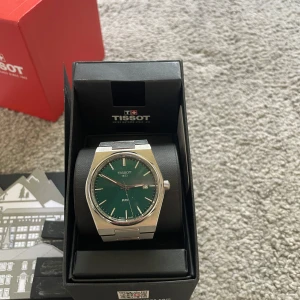 Tissot PRX klocka med grön urtavla - Stilren Tissot PRX klocka med grön urtavla och silverfärgat armband i rostfritt stål. Klockan har en klassisk rund form, datumvisning och snyggt integrerad länk. Perfekt accessoar för dig som gillar modern och tidlös design. Två extra länkar med följer 