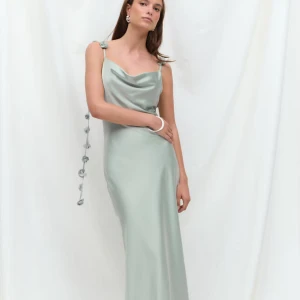 Ljusgrön långklänning med rosettdetaljer - Superfin ljusgrön långklänning i satinliknande material med smala axelband och draperad urringning. Axelbanden har unika rosettdetaljer som hänger ner längs ryggen. Helt ny 