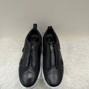 Valentino Garavani svarta sneakers - Svarta sneakers från Valentino Garavani i skinn med vita sulor dekorerade med ikoniska nitar. Snygg minimalistisk design utan synlig snörning och diskreta detaljer. Perfekta för dig som gillar lyxiga och stilrena skor med edge.