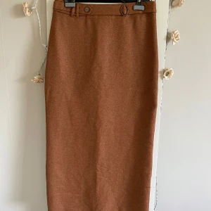 Brun långkjol från Akasya - Snygg brun långkjol från Akasya med klassisk rak passform och bälte i midjan. Kjolen har en enkel design utan mönster och är tillverkad i ett mjukt tyg som känns lite som ull. Perfekt för dig som gillar stilrena och tidlösa plagg.