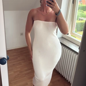 Vit ribbad axelbandslös långklänning - Supersnygg axelbandslös långklänning i ribbad, stretchig vit bomullsmix. Klänningen sitter tight och framhäver figuren, perfekt för dig som gillar minimalistisk och clean stil. Enkel att styla med smycken eller sneakers för en cool look. Se defekter sista bilder går säkert att få bort med klor el vanish o dylikt. Väldigt stretchig o den har en hummi rensa inuri vid bröstet så klänningen ej åker ner.