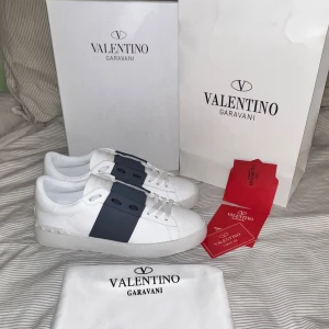 Valentino Garavani Open sneakers vit/blå - Snygga Valentino Garavani Open sneakers i vitt skinn med bred marinblå rem över vristen. Klassisk låg modell med rund tå, vita snören och diskreta nitar på hälen. Kommer med originalkartong, dustbag och äkthetskort. Obs lnte 0rglnal!