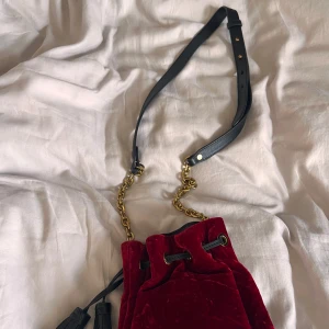 Röd sammet axelväska Polo Ralph Lauren - Säljer denna superfina axelväska i rött sammet från Polo Ralph Lauren. Väskan har guldfärgad kedja, svart justerbart axelband i skinn och snygga tofsdetaljer. Aldrig använd heller