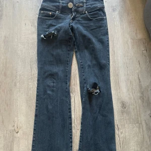 Mörka bootcut jeans med slitningar - Säljer ett par mörkblå bootcut jeans, egengjorda hål på knät och högre upp vid låret. Hålen nere vid hälarna har gått sönder med tiden men inget man tänker på.