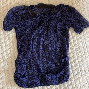 Lila blus med leopardmönster - Säljer en luftig och transparent lila blus med svart leopardmönster. Blusen har korta puffärmar och rund halsringning. Perfekt för dig som vill sticka ut med ett coolt mönster och en trendig färg. Passar lika bra till jeans som till kjol. Har inget lapp men passar som en L/M