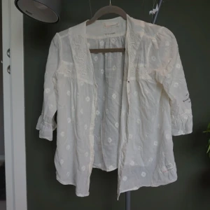 Vit Odd Molly blus med broderi - Superfin vit blus från Odd Molly med broderade detaljer och diskret mönster. Lätt och luftig i bomull, med trekvartsärmar och broderad text på ärmen. 