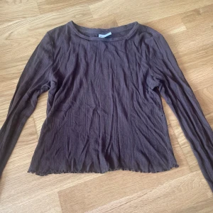 Brun ribbad somrig långärmad tröja  - Brun långärmad tröja i storlek S. Tröjan har ett ribbat och diskret mönstrat tyg med lätt vågig kant nertill. Den är tunn och stretchig, perfekt för lager-på-lager och funkar året runt, superfint. Från vero Moda 