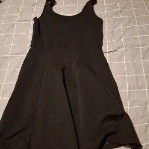 Svart kort klänning från H&M Divided - En svart, ärmlös kortklänning från H&M Divided med klassisk rund halsringning och lätt utställd kjol. Enkel och stilren design som passar perfekt till sneakers eller boots. Materialet känns mjukt och följsamt.