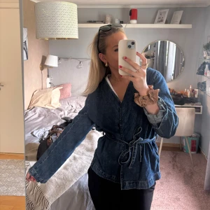 Blå omlott jeansjacka med knytband - Säljer en snygg blå jeansjacka i omlottmodell med knytband i midjan. Jackan har lång ärm och är tillverkad i klassiskt denimtyg. Skriv för fler bilder om det önskas ❤️nypris 1000 kr