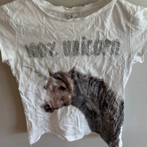 Vit topp med unicorn-tryck och pärlor - Cool vit topp från H&M med korta ärmar och texten '100% unicorn' i glittriga pärlor. Stor unicorn-tryck framtill med horn i pärldetaljer. Perfekt för dig som älskar magiska motiv och vill sticka ut lite extra.