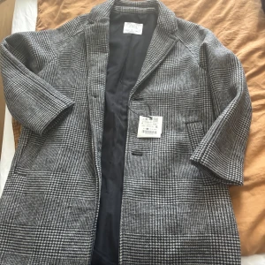 Rutig kappa från Zara, svartvit - Snygg rutig kappa från Zara i svart och vitt. Klassisk modell med krage och knappar framtill. Fodrad insida och två fickor framtill. 