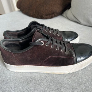 Svarta lanvins - Snygga lanvins i mörk och brun  mocka med svarta skinn-detaljer på tån och svarta skosnören. Skorna har vit platt sula och rund tå. Perfekta för dig som gillar en stilren men ändå unik look. Storlek 44, och sulan är 30cm 