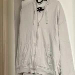 Ljusgrå hoodie med dragkedja från H&M - Ljusgrå hoodie från H&M i relaxed fit med dragkedja framtill, huva med snörning och två fickor. Tillverkad i mjuk bomullsblandning, perfekt för chill dagar. Långärmad och enkel stil som funkar till det mesta. Den är i storlek M men passar eventuellt S, tecken på användning 4-5 gånger. Ni kan köpa direkt eller kontakta mig för övriga frågor! 
