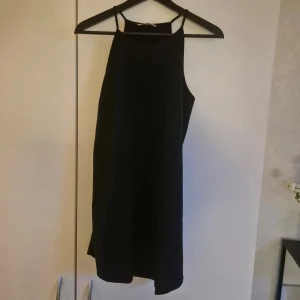 Svart kort klänning från Supré - En stilren, svart, kortklänning som är något längre baktill. Från Supré, inköpt i Australien. Raka tunna axelband och hög halsringning. Klänningen har loosefit. 