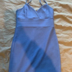 Blå kort klänning Miss Selfridge - Snygg blå kort klänning från Miss Selfridge med smala axelband och v-ringad överdel. Klänningen har en figurnära passform och är tillverkad i ett strukturerat tyg som ger en cool känsla. Perfekt för dig som vill sticka ut med en enkel men stilren look.