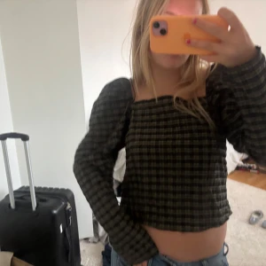Rutig croppad blus med puffärm - Säljer en croppad rutig blus i mörkgrönt och svart med fyrkantig ringning och långa puffärmar. Toppen har en loose fit och ger en trendig vibe till din outfit. Perfekt att styla med jeans för en cool look.