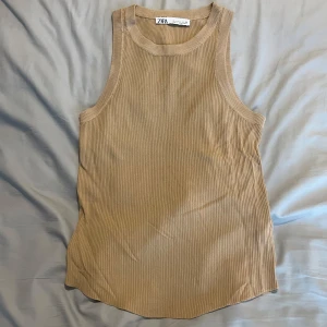 Beige ribbad linnetopp från Zara - Säljer en beige ribbad linnetopp från Zara i storlek L. Toppen har en klassisk rund halsringning och är ärmlös med breda axelband. Perfekt för en clean och avslappnad look, lätt att matcha med jeans eller kjol.
