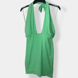 Grön kort klänning från Bik Bok - Superfin grön kort klänning från Bik Bok med djup v-ringning och knyt i nacken. Klänningen är ärmlös och har en snygg öppen rygg. Perfekt för varma dagar när du vill sticka ut lite extra.