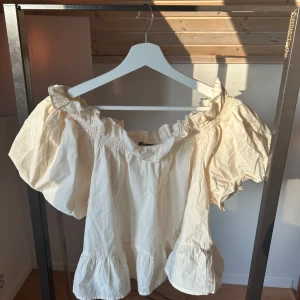 Vit offshoulder blus med volang - Supersöt vit blus med offshoulder och volangdetaljer runt halsringningen och ärmsluten. Luftig modell med korta puffärmar och rynk vid axlarna. Köpt från Gina när vissa varor skulle rensas och sluta säljas. Storlek XL men passar super bra på mig som vanligtvis har Xs/S. Rekommenderas om man bär S/M. Kontakta mig om ni vill ha en bild på hur den ser ut på.🥰 ljus gul färg 
