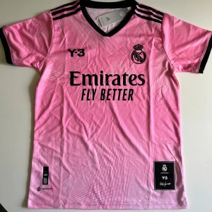 Real Madrid x Y-3 rosa fotbollströja S - Snygg Real Madrid fotbollströja i samarbete med Y-3 och Adidas. Tröjan är rosa med svarta detaljer, har korta ärmar och V-ringning. Tryck med 'Emirates Fly Better' och klubbmärke på bröstet. Tillverkad i lätt och ventilerande AEROREADY-material.
