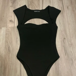 Svart body  - Svart body  med cool cut out-detalj över bröstet och breda axelband. Snygg, figurnära passform som framhäver siluetten. Perfekt att styla med jeans eller kjol för en trendig look.