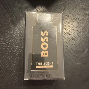 Boss The Scent Eau de Toilette - Boss The Scent Eau de Toilette är en elegant herrparfym med noter av ingefära, exotisk maninka och läder. Flaskan är svart med guldiga detaljer och rymmer 50 ml. Perfekt för dig som gillar en sofistikerad och maskulin doft. Hör av er vid minsta lilla fråga eller fundering. Helt ny och oöppnad 