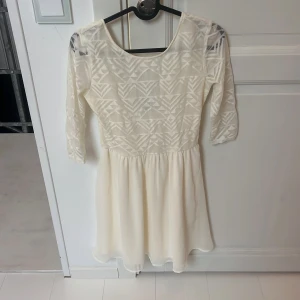 Vit kortklänning  - Supersöt vit kortklänning från Divided med trekvartsärm och geometriskt mönster upptill. Kjolen är lätt och flowy, perfekt för vår och sommar. Klänningen har rund halsringning och är i ett tunt, skönt material.