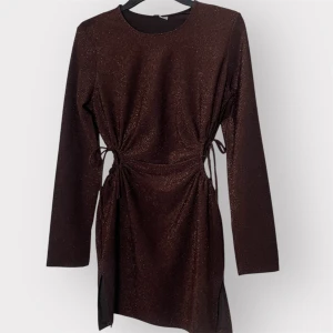 Glittrig brun kortklänning H&M Divided - Supersnygg brun glittrig kortklänning från H&M Divided med långa ärmar och cool snörning i midjan. Klänningen har en lätt figurnära passform och slitsar i sidorna. Perfekt för dig som vill sticka ut med lite extra glitter.