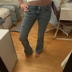 Bootcut ljusblå jeans med slitningar - Säljer ett par ljusblå bootcut jeans med snygga slitningar på knäna och låret. Jeansen har låg midja, klassiska fem fickor och är i mjukt denimtyg. Perfekta för en avslappnad och trendig look. Hålen är självgjorda! Midjemått- 35cm tvärsöver, innerben- 81cm