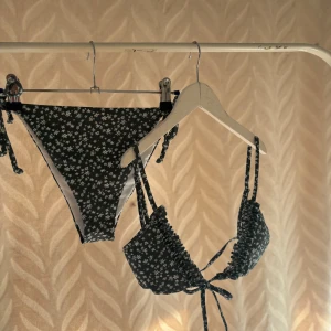 Grön  blommig bikini med volang - Helt oanvänd Supersöt grön bikini med vita blommor och volangdetaljer på överdelen. Både över- och underdel har knytband i sidorna för perfekt passform. Perfekt för stranden eller poolen i sommar!