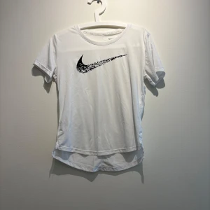 Vit Nike Dri-Fit t-shirt XS - Vit Nike Dri-Fit t-shirt i sportig modell med svart swoosh-logga framtill. T-shirten har rund hals, korta ärmar och är tillverkad i ett lätt och svalt funktionsmaterial som passar perfekt för träning. Enkel och clean design med något längre baksida.