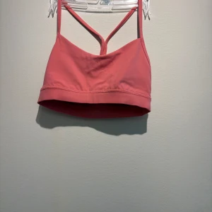 Rosa sportig linnetopp från Lululemon - Säljer en rosa linnetopp från Lululemon med smala axelband som korsas i ryggen. Toppen är croppad och har en sportig look, perfekt för träning. Tillverkad i mjukt och stretchigt material som ger bra stöd och rörelsefrihet.