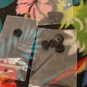 Svarta knappar från Stone Island - Säljer svarta knappar från Stone Island, perfekta som reservdelar till jackor eller byxor. Knapparna är runda med texten 'Stone Island' ingraverad och levereras i små plastpåsar. Snygg och stilren design som passar streetwear.