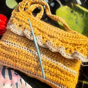 Gul handvirkad axelväska med volang - Unik handvirkad axelväska i varm gul och beige ton. Väskan har virkade ränder och en söt volangkant upptill. Den är gjord i mjukt garn med tvinnat axelband och passar perfekt för dig som gillar färg och personliga accessoarer.
