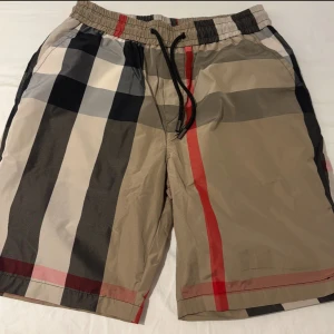 Beige rutiga shorts - Snygga beige shorts med klassiskt rutigt mönster i svart, vitt och rött. De har elastisk midja med svart snörning för skön passform. 